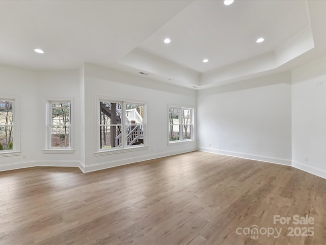 unfurnished living room featuring recessed lighting, a tray ceiling, baseboards, and wood finished floors