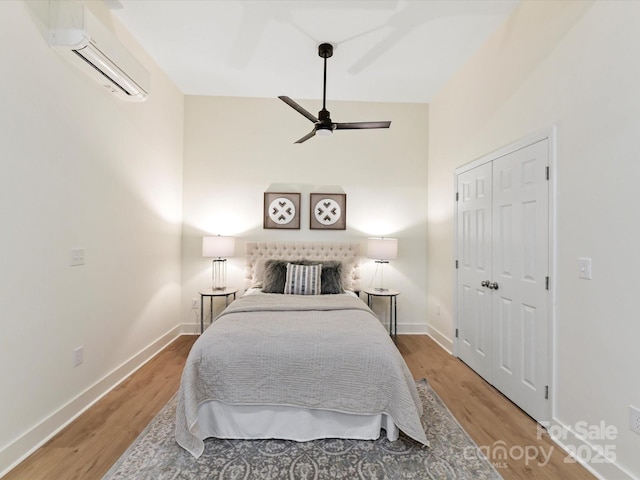 bedroom with a closet, an AC wall unit, baseboards, and wood finished floors