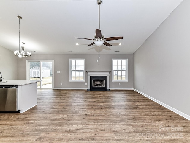 unfurnished living room with sink, ceiling fan with notable chandelier, and light wood-type flooring