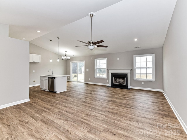 unfurnished living room featuring vaulted ceiling, sink, ceiling fan with notable chandelier, and light hardwood / wood-style flooring