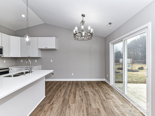 kitchen with lofted ceiling, sink, white cabinetry, wood-type flooring, and decorative light fixtures