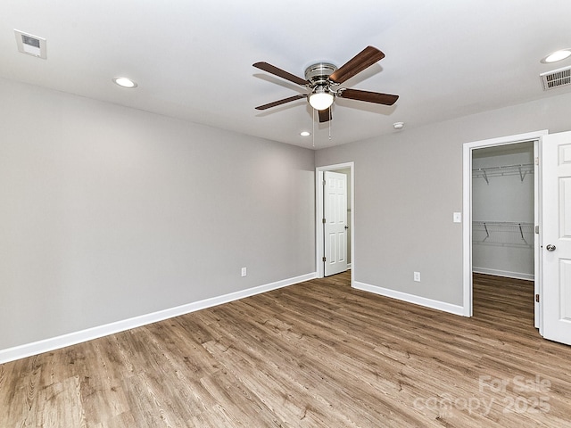 unfurnished bedroom with hardwood / wood-style floors, a walk in closet, a closet, and ceiling fan