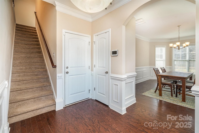 entryway featuring dark wood-type flooring, crown molding, and an inviting chandelier