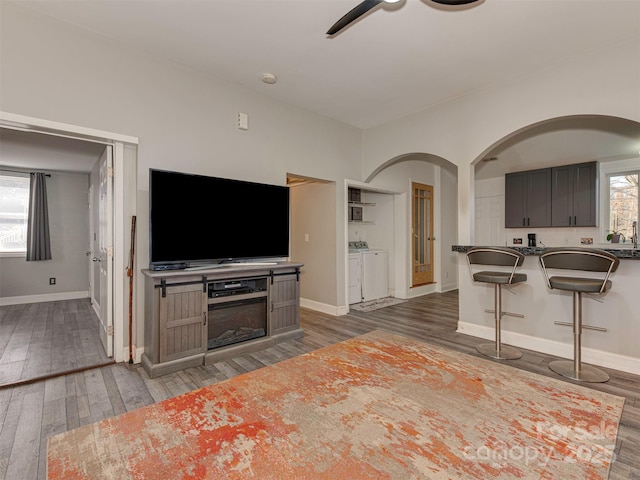 living room featuring arched walkways, a ceiling fan, baseboards, dark wood-style floors, and washer and clothes dryer