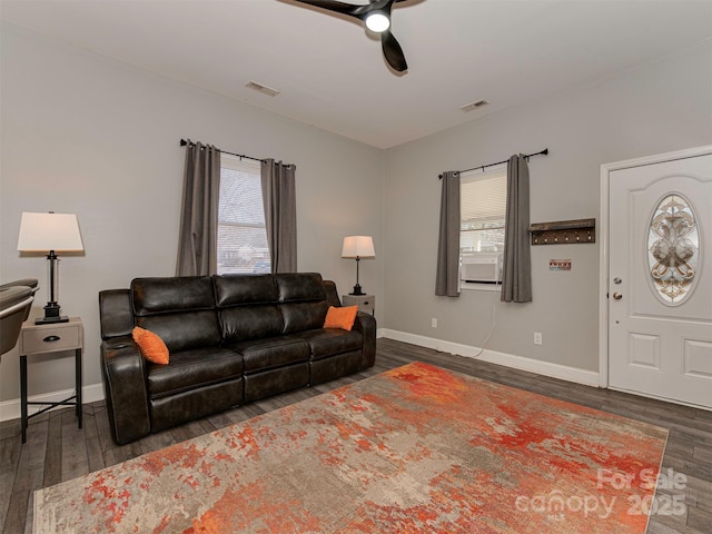 living room with dark wood-style floors, baseboards, visible vents, and ceiling fan