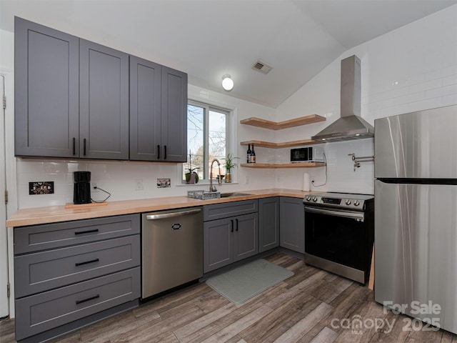 kitchen with wall chimney range hood, gray cabinets, sink, and appliances with stainless steel finishes