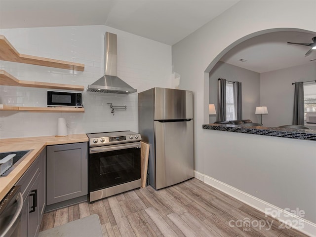 kitchen featuring open shelves, stainless steel appliances, gray cabinets, butcher block countertops, and wall chimney exhaust hood