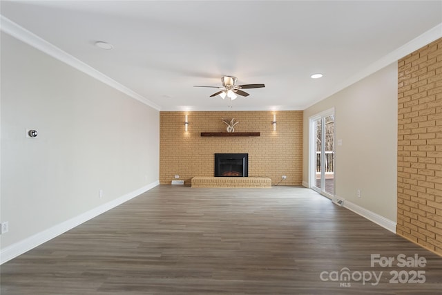 unfurnished living room featuring crown molding, dark wood-type flooring, ceiling fan, brick wall, and a brick fireplace