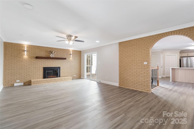 unfurnished living room featuring a fireplace, ornamental molding, wood-type flooring, and brick wall