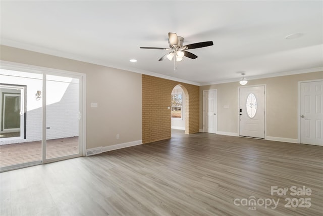 unfurnished living room featuring crown molding, hardwood / wood-style flooring, ceiling fan, and brick wall