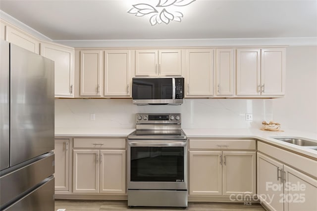 kitchen with tasteful backsplash, appliances with stainless steel finishes, cream cabinets, and light hardwood / wood-style flooring