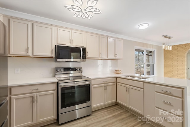 kitchen with pendant lighting, sink, appliances with stainless steel finishes, cream cabinets, and light wood-type flooring