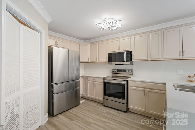 kitchen with sink, crown molding, appliances with stainless steel finishes, light hardwood / wood-style floors, and cream cabinetry