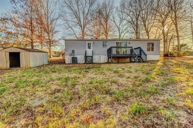 rear view of property with a wooden deck, a lawn, central AC unit, and a storage shed