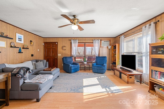 living room with wooden walls, light wood-type flooring, ceiling fan, crown molding, and a textured ceiling