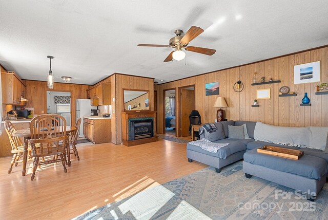 living room featuring wooden walls, washer / clothes dryer, ornamental molding, ceiling fan, and light hardwood / wood-style floors