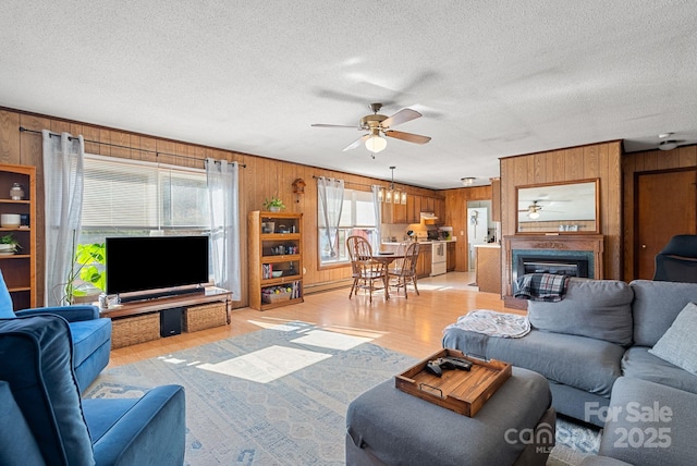 living room featuring ceiling fan, light wood-type flooring, a textured ceiling, and wooden walls