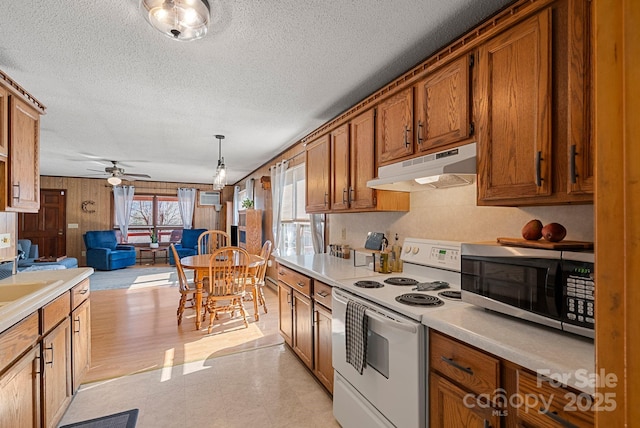 kitchen with pendant lighting, ceiling fan, a textured ceiling, white electric stove, and wood walls