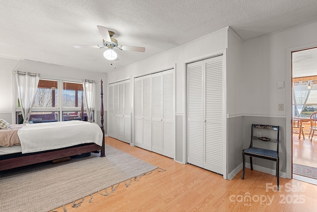 bedroom with multiple closets, multiple windows, light hardwood / wood-style flooring, and a textured ceiling