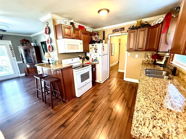 kitchen with sink, a breakfast bar area, light stone counters, and white appliances