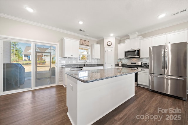 kitchen featuring stainless steel appliances, dark stone counters, a kitchen island, and white cabinets