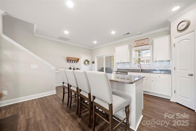 kitchen with stone countertops, tasteful backsplash, white cabinets, a kitchen breakfast bar, and a center island