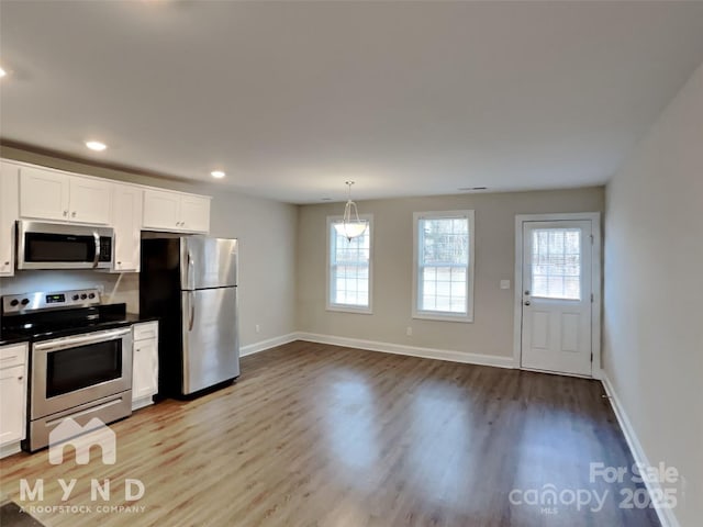 kitchen with stainless steel appliances, pendant lighting, white cabinets, and light wood-type flooring