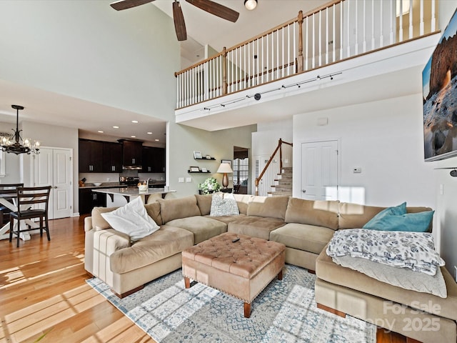 living room with a towering ceiling, ceiling fan with notable chandelier, and light wood-type flooring