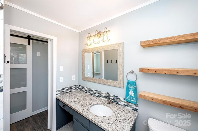 bathroom with hardwood / wood-style floors, backsplash, vanity, toilet, and crown molding