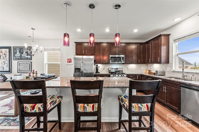 kitchen featuring stone countertops, appliances with stainless steel finishes, a center island, a sink, and backsplash