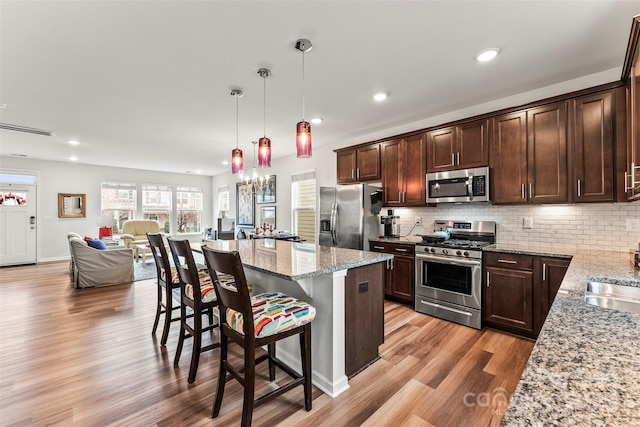 kitchen with a breakfast bar, backsplash, light wood-style flooring, appliances with stainless steel finishes, and dark brown cabinetry