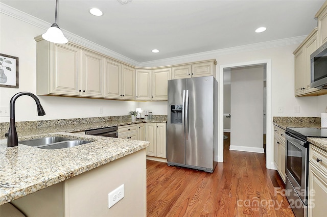 kitchen with pendant lighting, light wood finished floors, cream cabinets, appliances with stainless steel finishes, and a sink