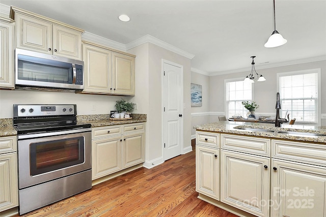 kitchen with light wood-style flooring, stainless steel appliances, ornamental molding, cream cabinetry, and pendant lighting