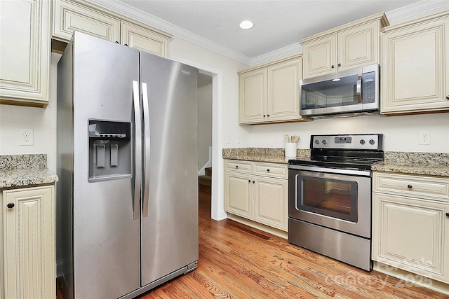 kitchen with stainless steel appliances, light wood-style floors, ornamental molding, and cream cabinets