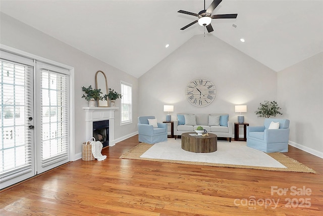 living room featuring light wood-style floors, a fireplace, high vaulted ceiling, and a ceiling fan