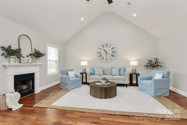 living area with high vaulted ceiling, a fireplace, wood finished floors, a ceiling fan, and baseboards