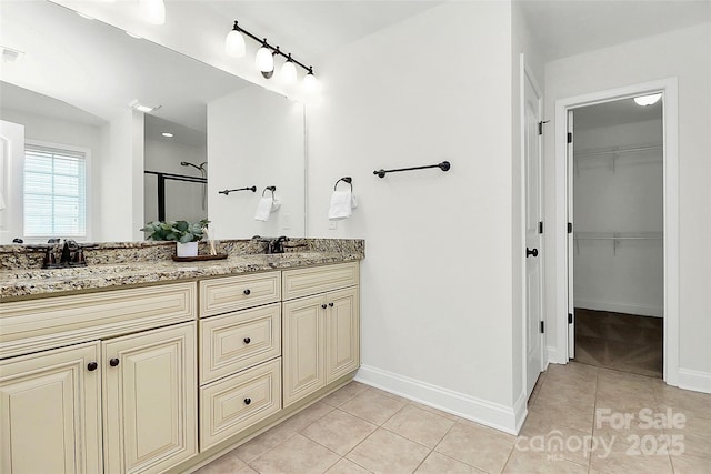 bathroom with tile patterned flooring, a sink, baseboards, double vanity, and a walk in closet