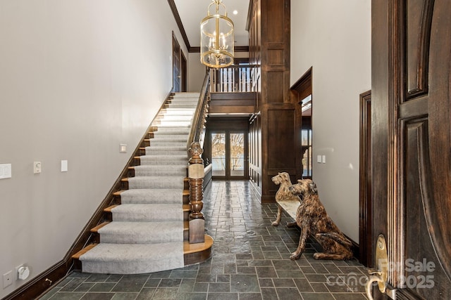 stairway with a notable chandelier, crown molding, stone tile flooring, a towering ceiling, and baseboards