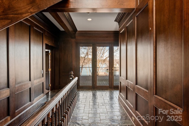 mudroom with ornamental molding, a decorative wall, stone tile flooring, and french doors