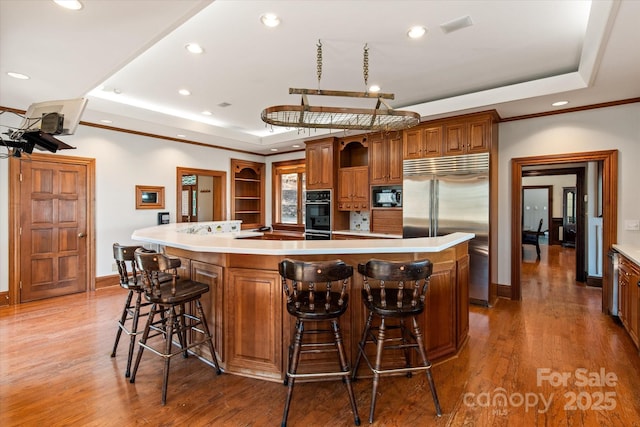 kitchen with a large island, a kitchen breakfast bar, a tray ceiling, light countertops, and black appliances