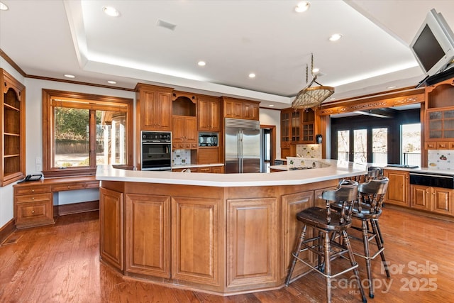 kitchen featuring a breakfast bar, a spacious island, a raised ceiling, light countertops, and built in appliances