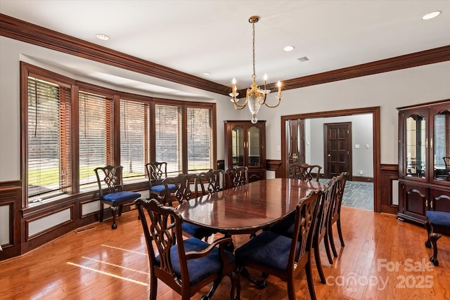 dining room with light wood-type flooring, a wainscoted wall, and ornamental molding