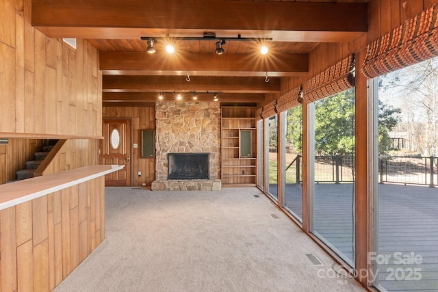 living area with carpet, beam ceiling, an outdoor stone fireplace, visible vents, and wood walls