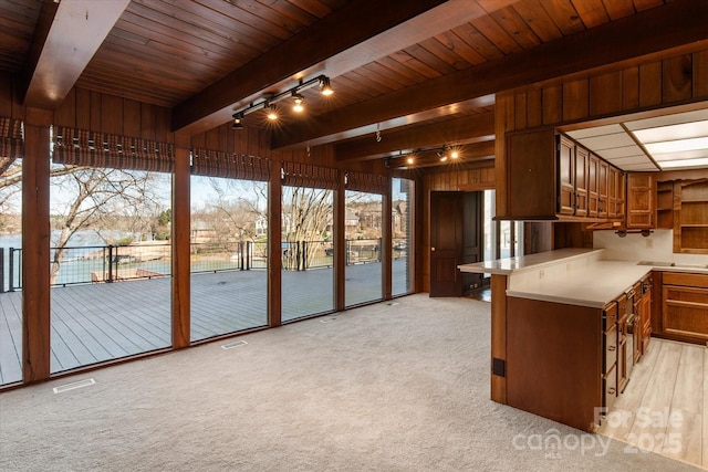 kitchen with light countertops, track lighting, beam ceiling, and brown cabinets