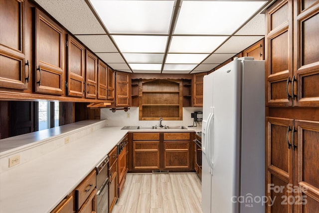 kitchen featuring open shelves, a paneled ceiling, light countertops, a sink, and white fridge with ice dispenser