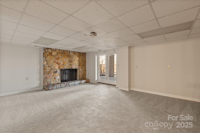 unfurnished living room with carpet floors, a fireplace, baseboards, and a drop ceiling