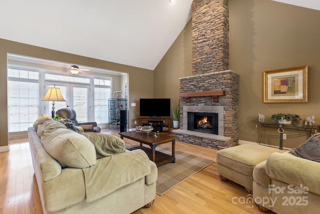 living room with ceiling fan, a stone fireplace, high vaulted ceiling, and light wood-type flooring