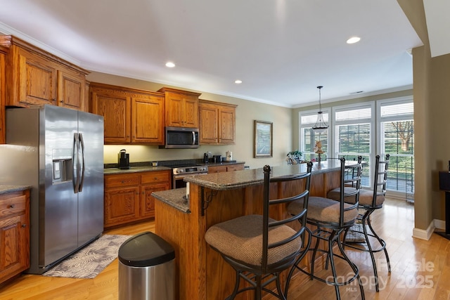 kitchen with hanging light fixtures, ornamental molding, a center island, stainless steel appliances, and light hardwood / wood-style flooring