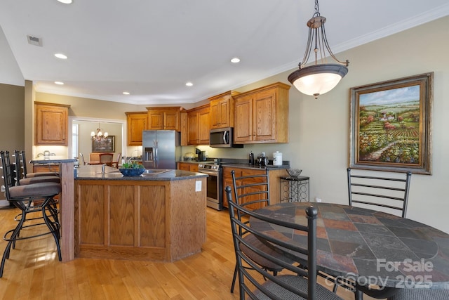 kitchen featuring pendant lighting, crown molding, stainless steel appliances, light hardwood / wood-style floors, and an island with sink