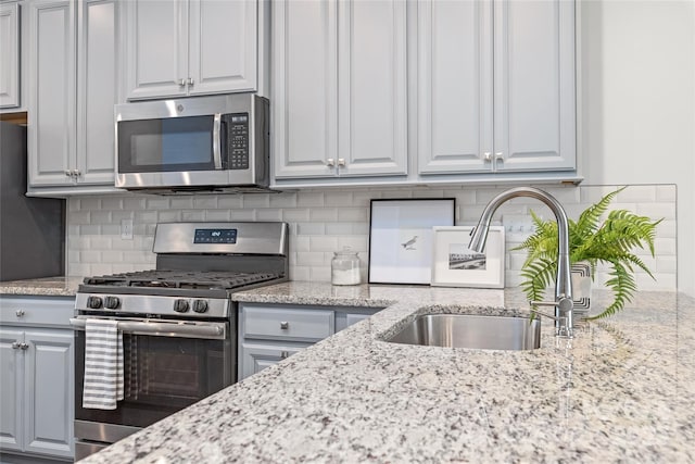 kitchen featuring sink, gray cabinets, stainless steel appliances, tasteful backsplash, and light stone countertops